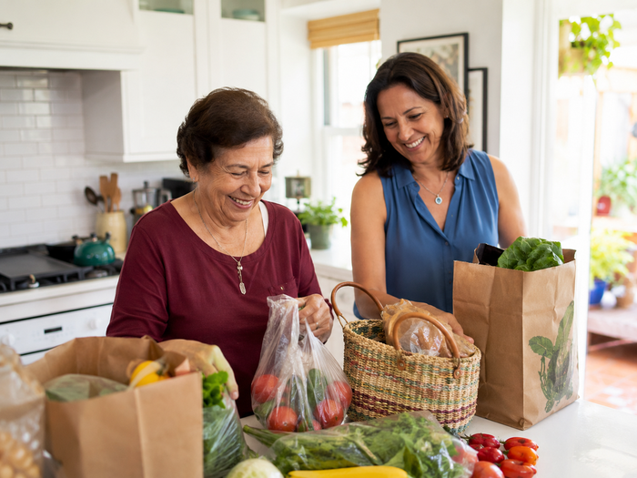 Duas mulheres organizando sacolas de compras juntas numa cozinha.